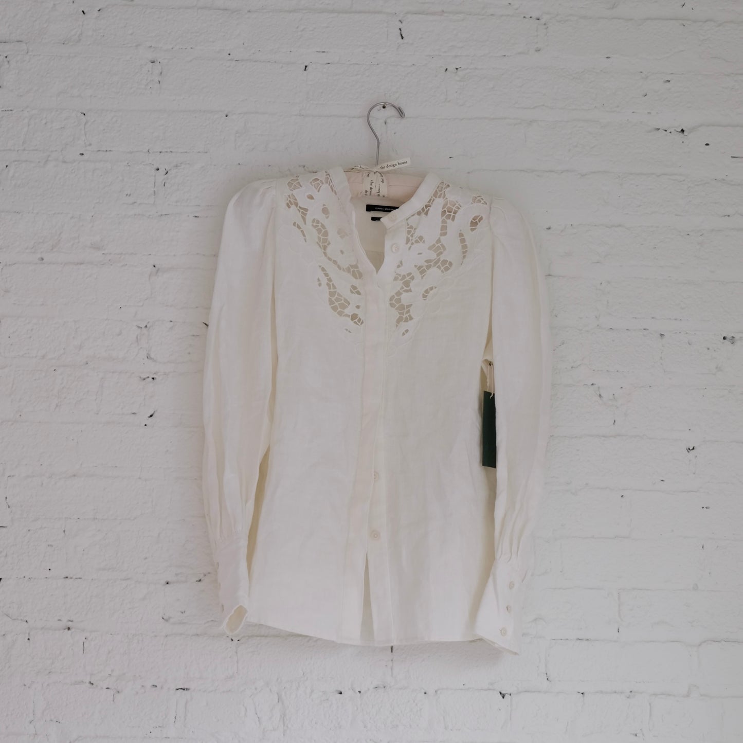 White Isabel Marant blouse with lace details on a hanger against a white brick wall.