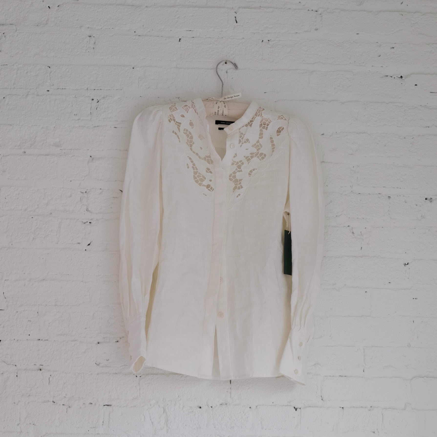 White Isabel Marant blouse with lace details on a hanger against a white brick wall.