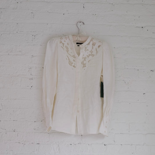 White Isabel Marant blouse with lace details on a hanger against a white brick wall.